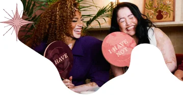 Winnie and a community member laughing together while holding "I HAVE" and "I HAVE NOT" signs
