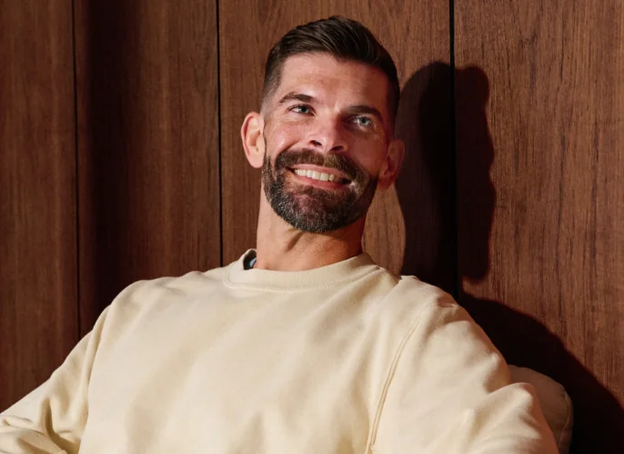 A man with a beard wearing a beige shirt and smiling